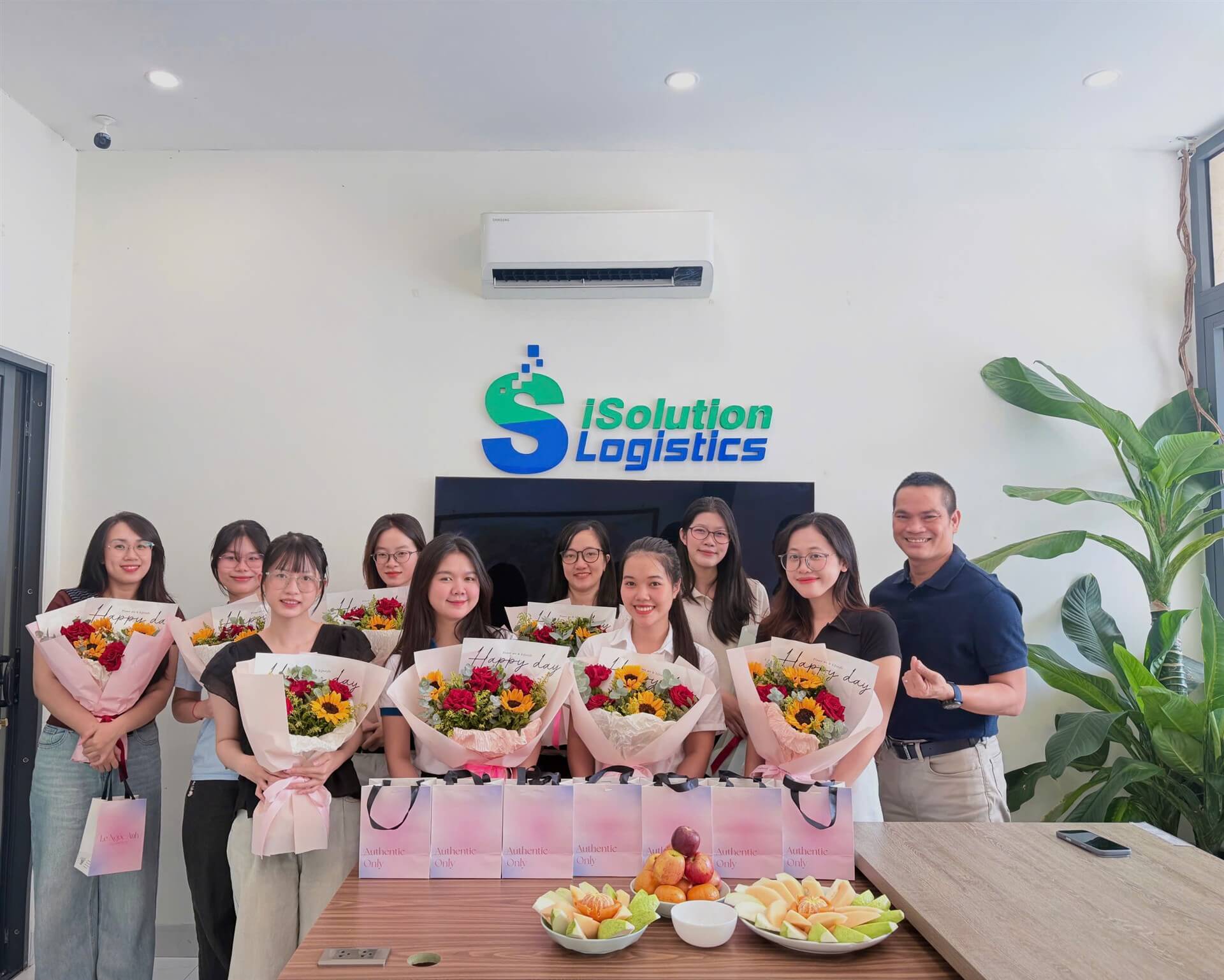 Female team members of ISOLUTION LOGISTICS holding flower bouquets with gift bags in front of them