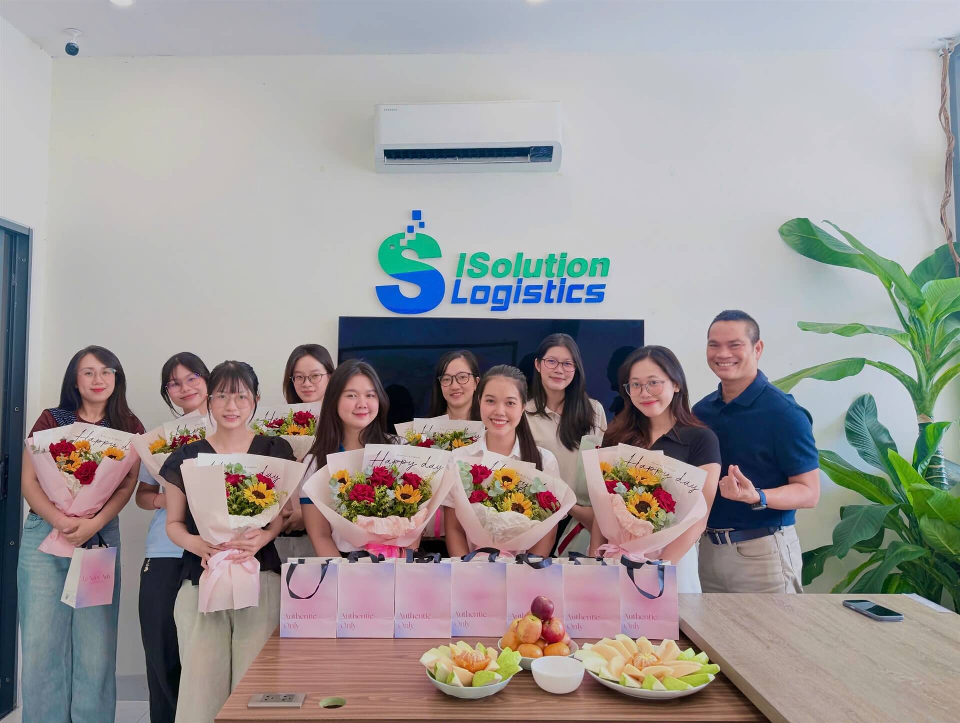 ISOLUTION LOGISTICS team holding bouquets in front of the company logo for Vietnamese Women's Day